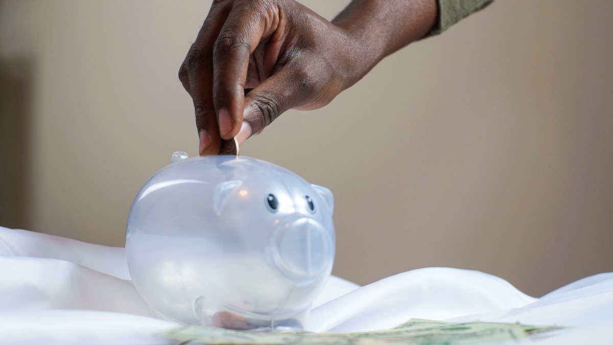 Hand dropping a coin into a clear piggy bank on a table