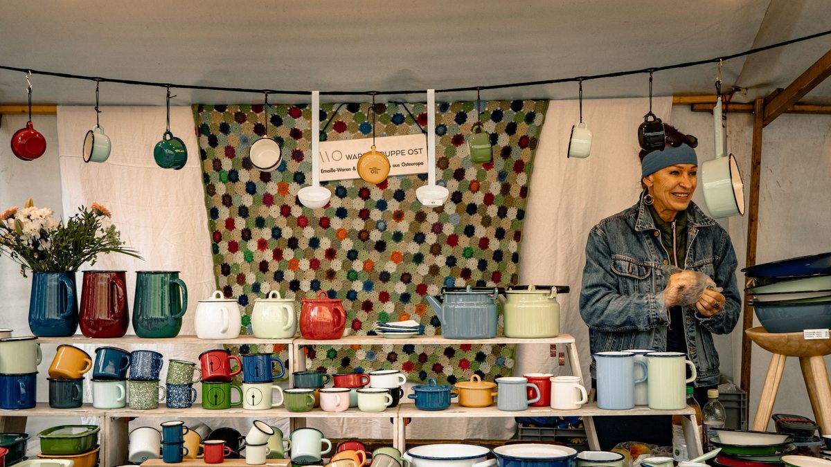 Smiling market vendor at a stall full of colorful handmade pottery