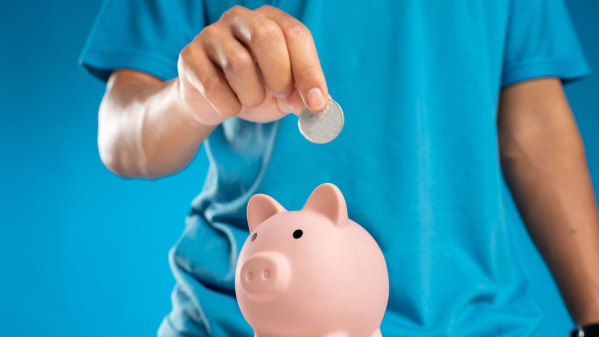 Hand dropping a coin into a pink piggy bank