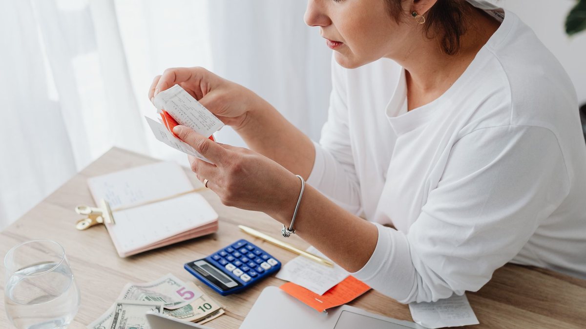 Young woman counting cash beside a laptop and calculator while budgeting