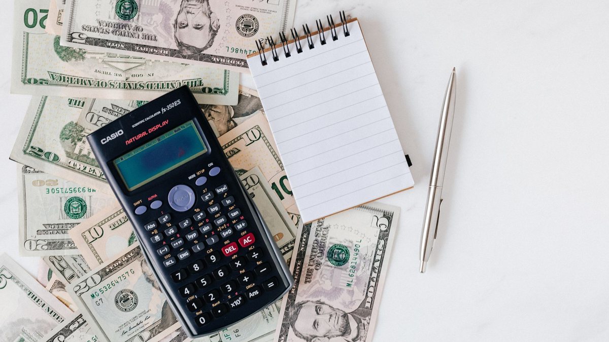 Calculator and a small notepad resting on a spread of U.S. dollar bills