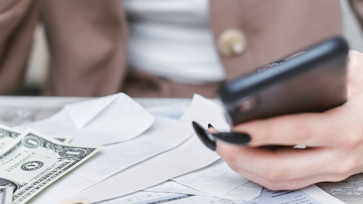 Woman holding a smartphone over a table with cash and paperwork