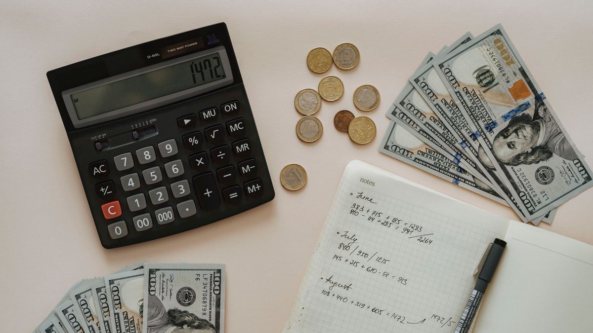 Calculator, coins, a notebook and dollar bills laid out on a desk for budgeting