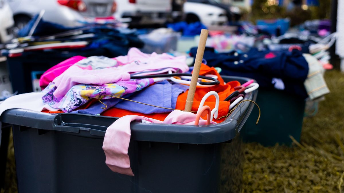 Plastic bins of colorful clothes set out on a lawn for a yard sale