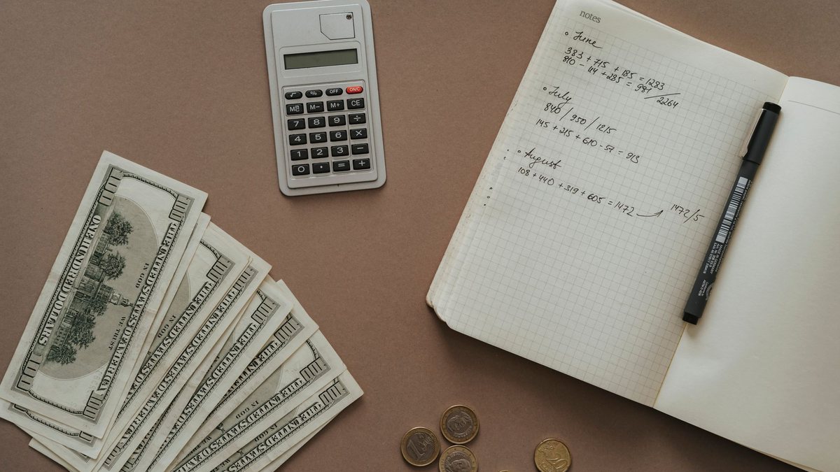 Notebook with handwritten notes beside a calculator, coins and dollar bills