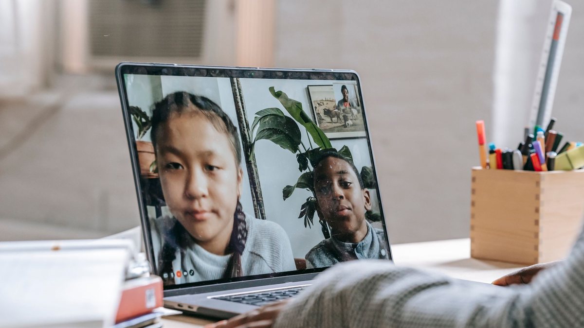 Tutor on a laptop video call teaching two smiling students