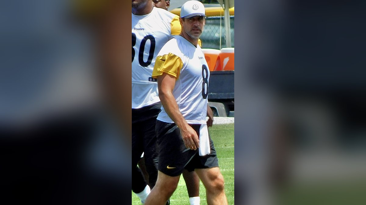Aaron Rodgers in a white Steelers practice jersey walks across the field at training camp in July 2025
