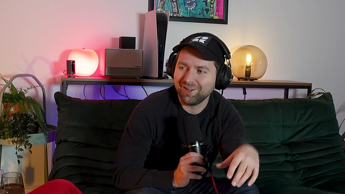 German Twitch streamer Adam Wolke in a black cap and headphones talking on a podcast couch