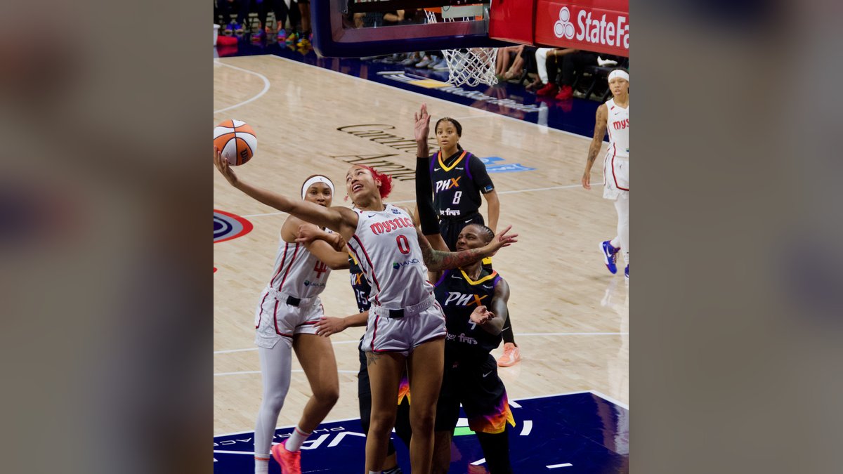 Washington Mystics center Shakira Austin in a white Mystics jersey reaching for a rebound under the basket against the Phoenix Mercury