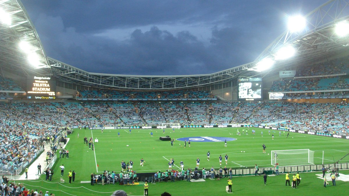 Players warm up on the floodlit field of Sydney's Olympic stadium under dark storm clouds as fans fill the lower stands
