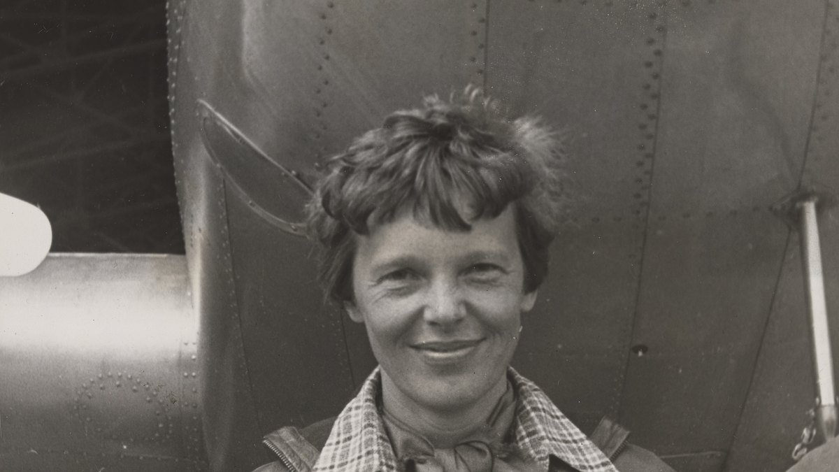 Amelia Earhart smiles while standing beneath the nose of her Lockheed Electra airplane in 1937
