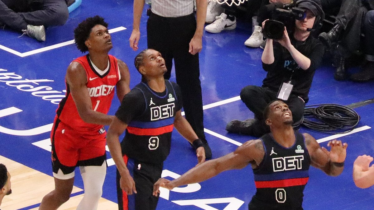 Rockets forward Amen Thompson in his red No. 1 road jersey looks up for a rebound beside Pistons players on an NBA court