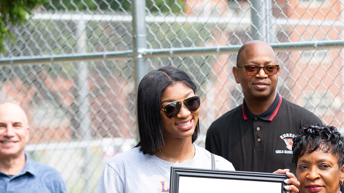 Angel Reese in sunglasses and an LSU T-shirt smiling beside community members at a basketball court dedication in Baltimore County