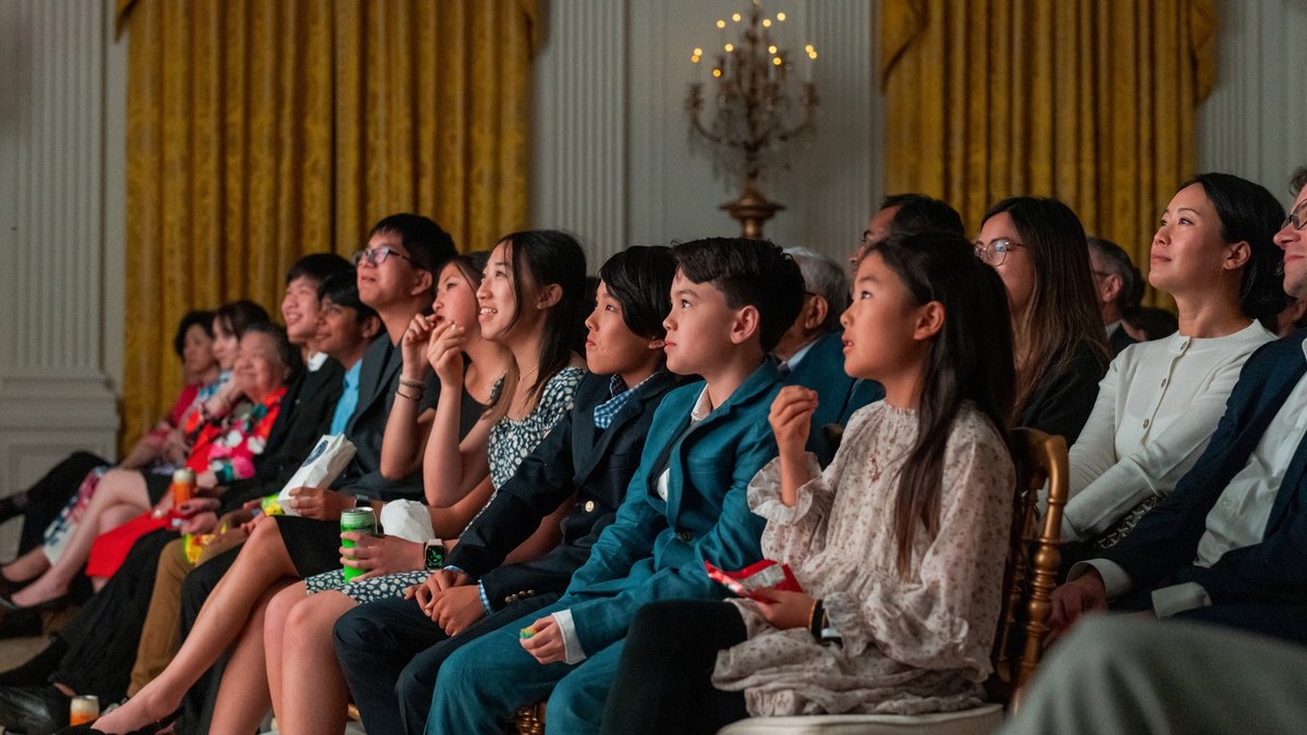 Asian American guests seated in the East Room of the White House listen and smile during a heritage month event