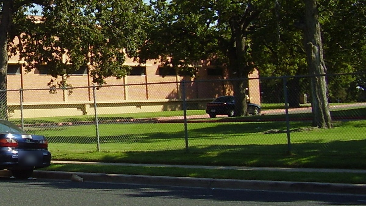 Parked cars along a fenced green lawn and brick building at Huston-Tillotson University in Austin