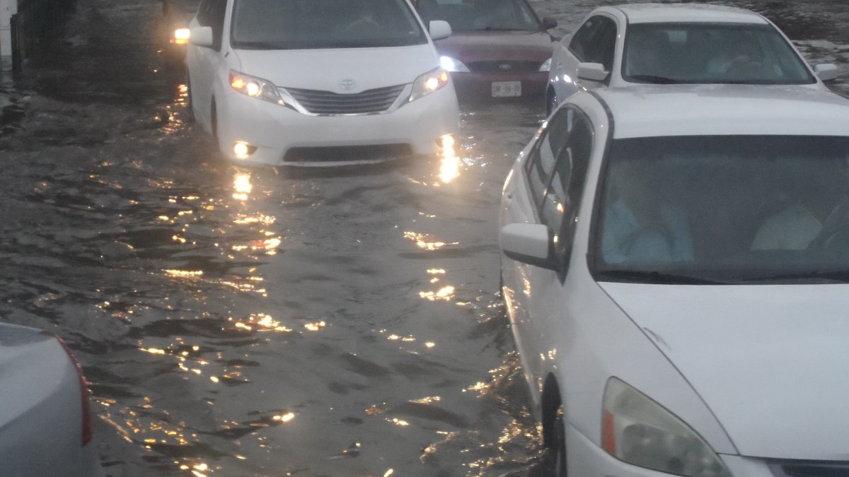 White cars with headlights on stuck in deep brown floodwater on a city street