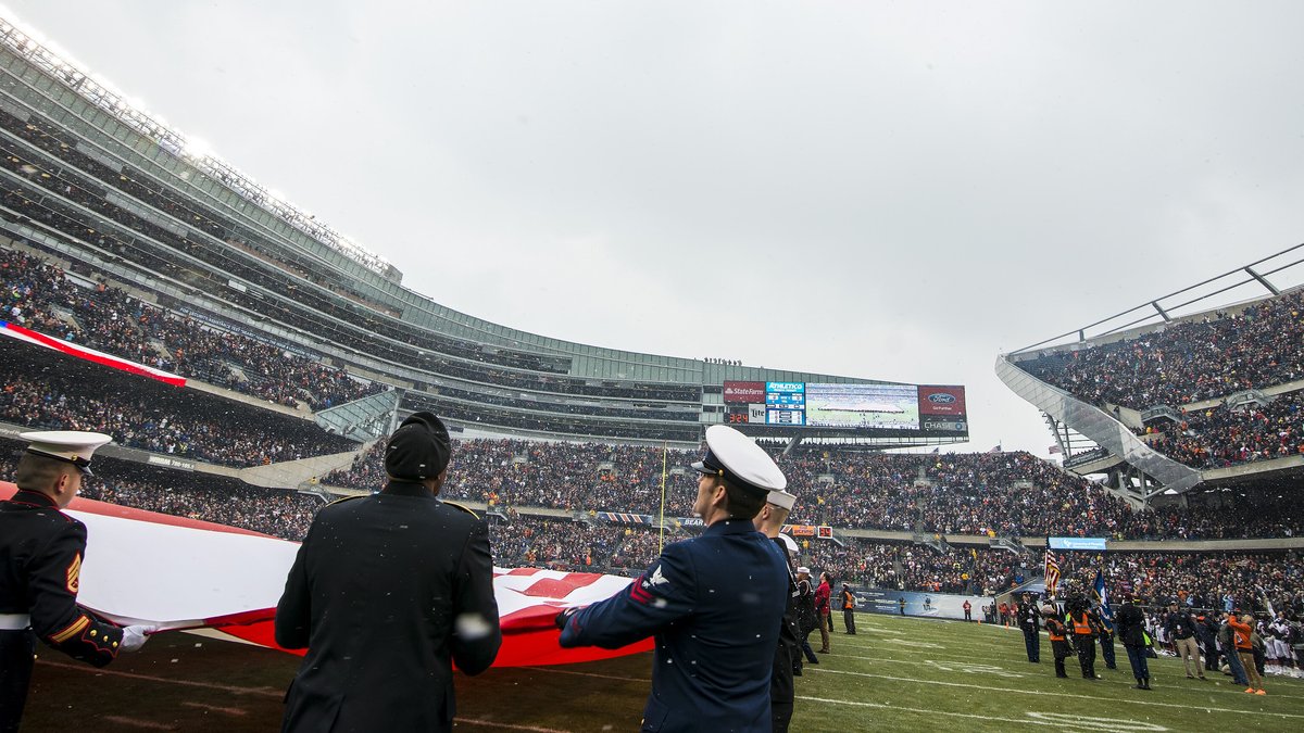 Service members unfurl a giant American flag on the field at Soldier Field as fans fill the stands before a Chicago Bears home game
