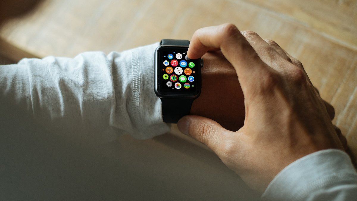 A hand tapping a black Apple Watch showing its app screen on a wrist in a white sleeve