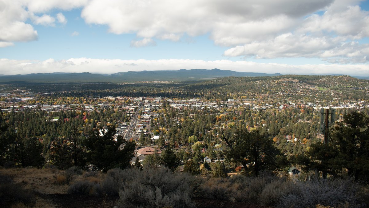 Wide view over the homes and pine trees of Bend, Oregon, from Pilot Butte with mountains on the horizon