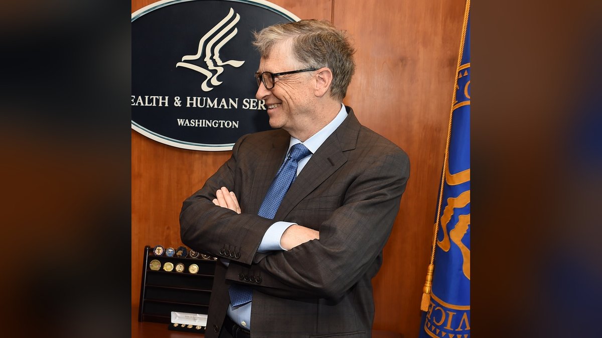 Bill Gates smiling with his arms crossed in a dark suit and blue tie