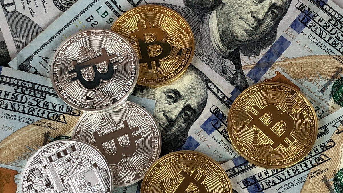 Gold and silver bitcoin tokens resting on a spread of U.S. hundred dollar bills