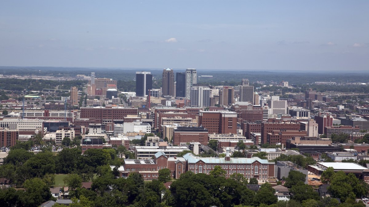 Downtown Birmingham, Alabama, skyline rising above tree-lined neighborhoods under a pale blue sky