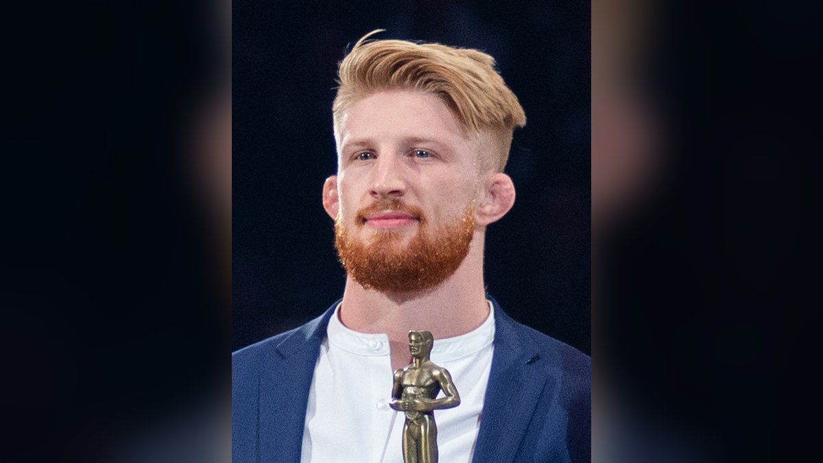 Bo Nickal in a navy blazer holds a small gold trophy during a Penn State wrestling ceremony