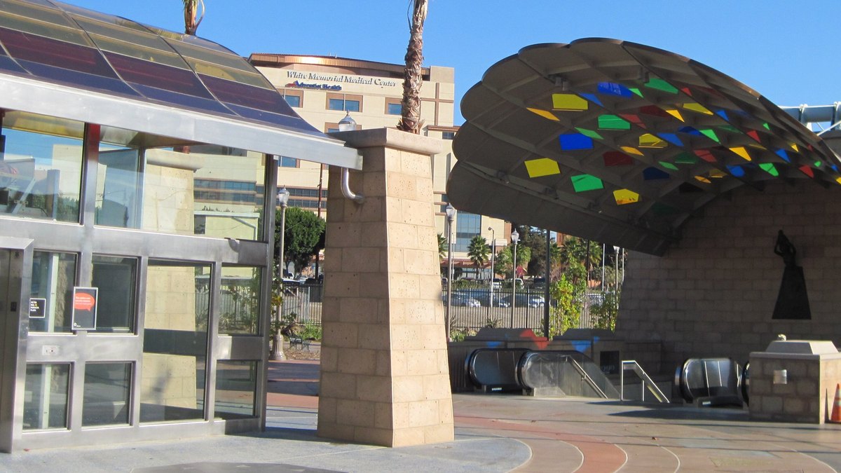 A colorful mosaic canopy arches over the entrance to the Mariachi Plaza transit station in Boyle Heights under a bright blue sky