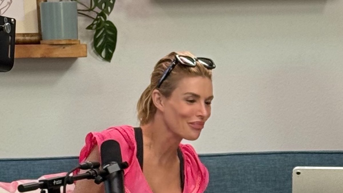 Brandi Glanville in a pink top smiling during a podcast taping