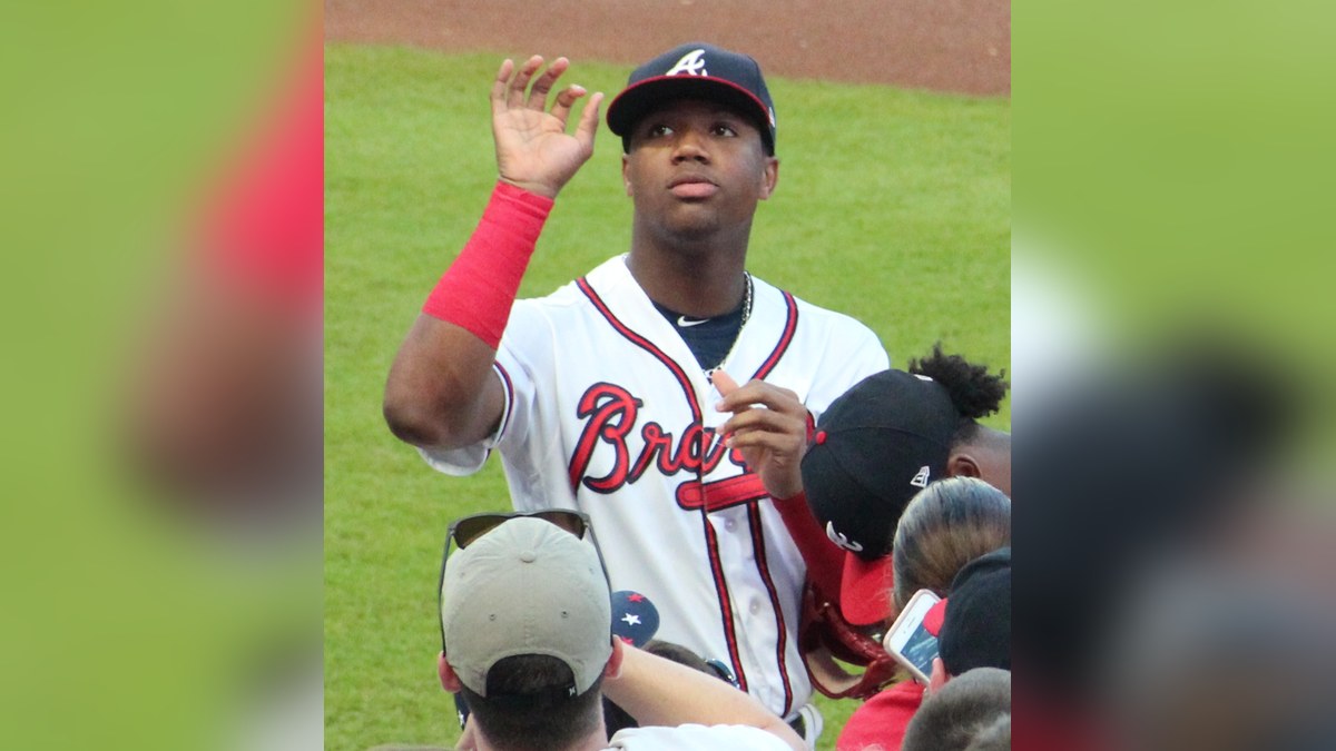 Ronald Acuña Jr. in a white Atlanta Braves jersey and cap waving to fans