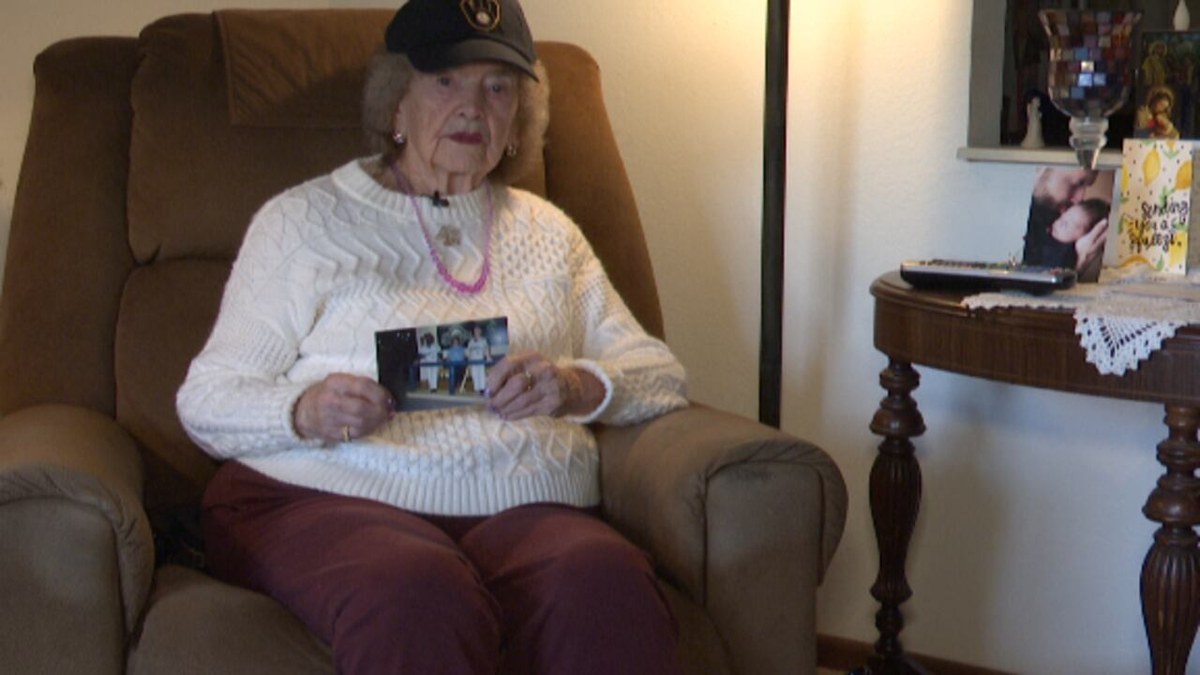 Joan Jehn, 96, in a Brewers cap and white sweater sitting in her armchair holding an old photo from a Brewers game