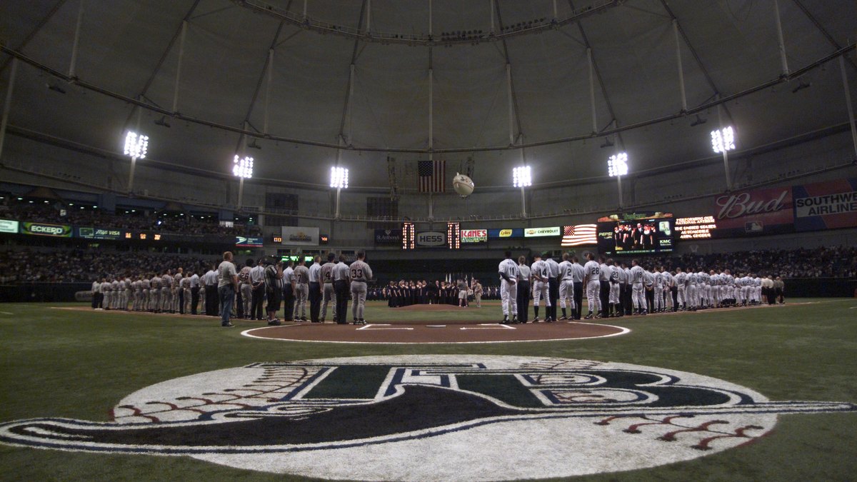 Players lined up along the baselines on the infield under the white dome roof of Tropicana Field before a baseball game