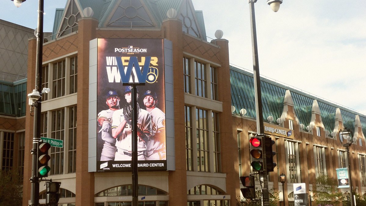 A tall video screen on a Milwaukee convention center shows Brewers players under a Win Our Way postseason banner