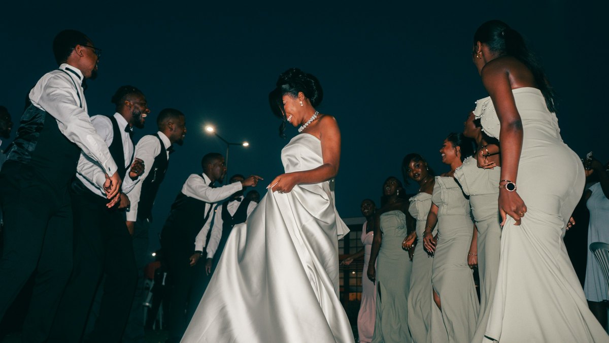 A bride in a white gown dancing with bridesmaids and groomsmen at a nighttime wedding party