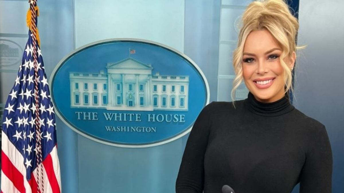 Britt McHenry smiling in a black turtleneck beside the White House seal in the press briefing room