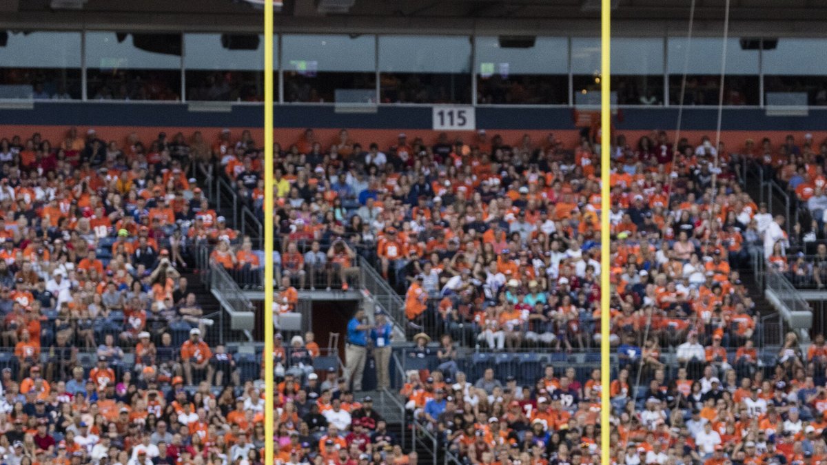 A packed crowd of Broncos fans in orange fills the stands behind the yellow goalposts at the stadium in Denver