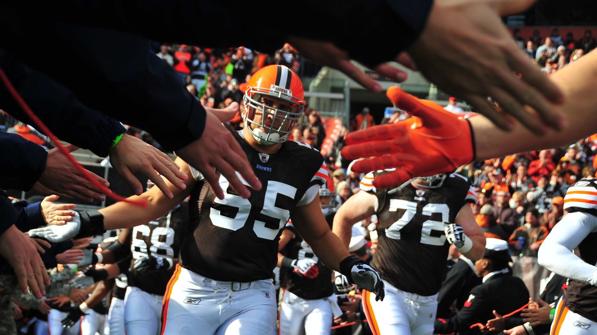 A Cleveland Browns player in an orange helmet runs through a line of service members slapping hands during pregame introductions at the Browns' home stadium