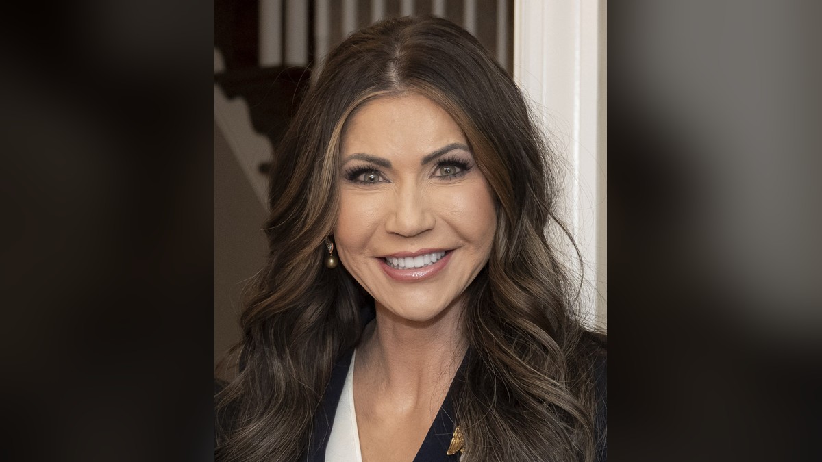 Kristi Noem smiling in a navy blazer with her long dark hair down