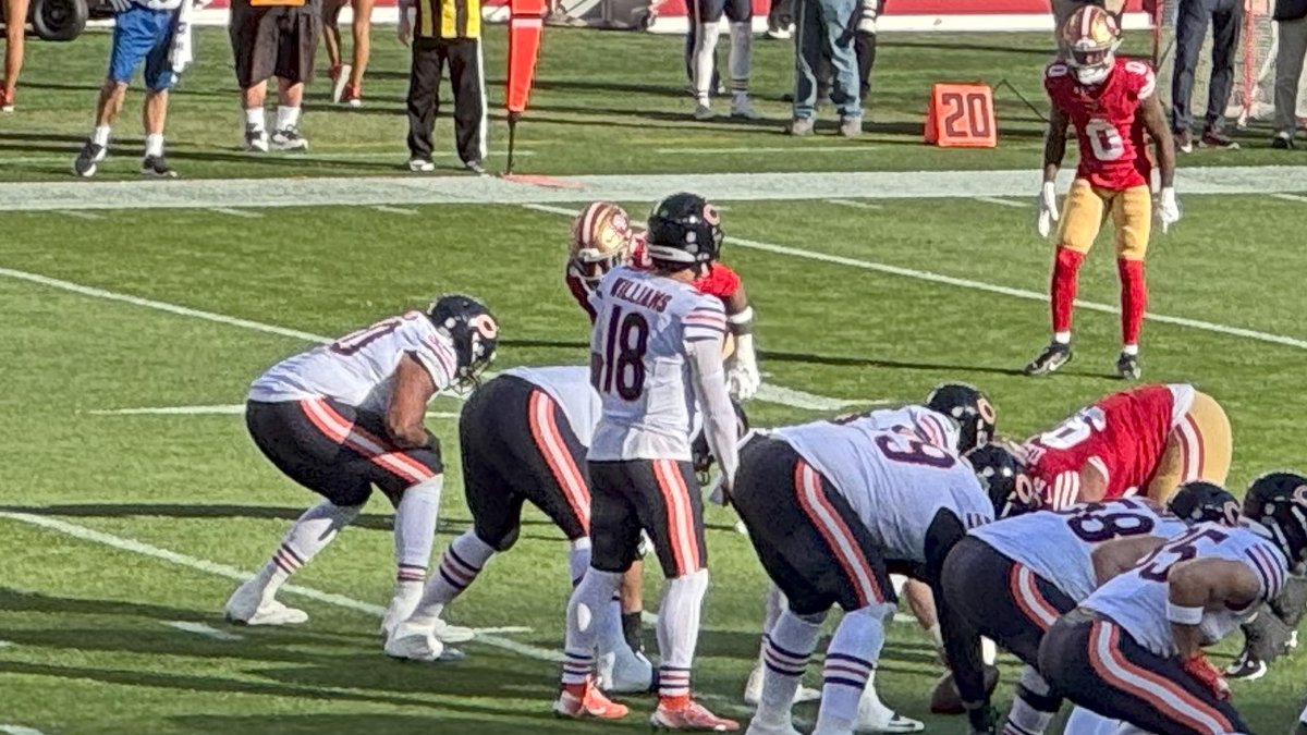 Bears quarterback Caleb Williams in his white No. 18 jersey stands in the shotgun behind his offensive line during a game against the 49ers