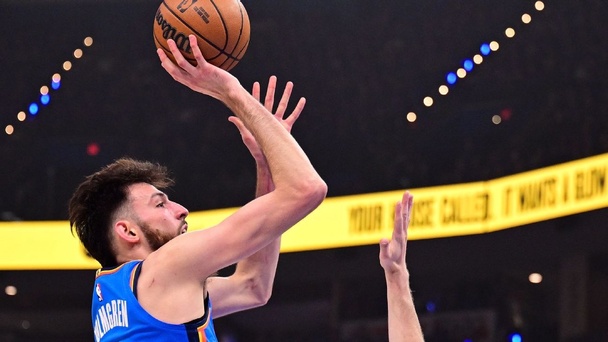 Chet Holmgren in a blue Oklahoma City Thunder jersey rises for a jump shot over a defender's outstretched hand
