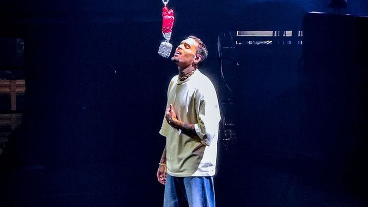Chris Brown singing on a dark stage beneath a hanging crystal microphone