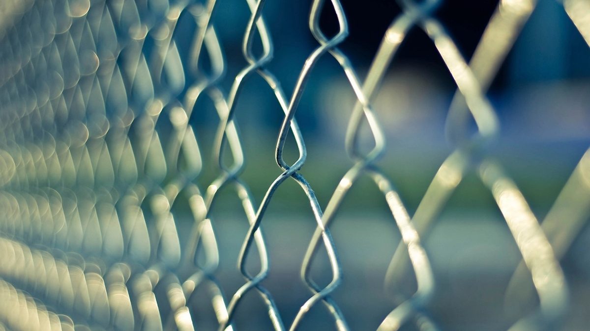Close view of a chain-link security fence against a blurred blue background