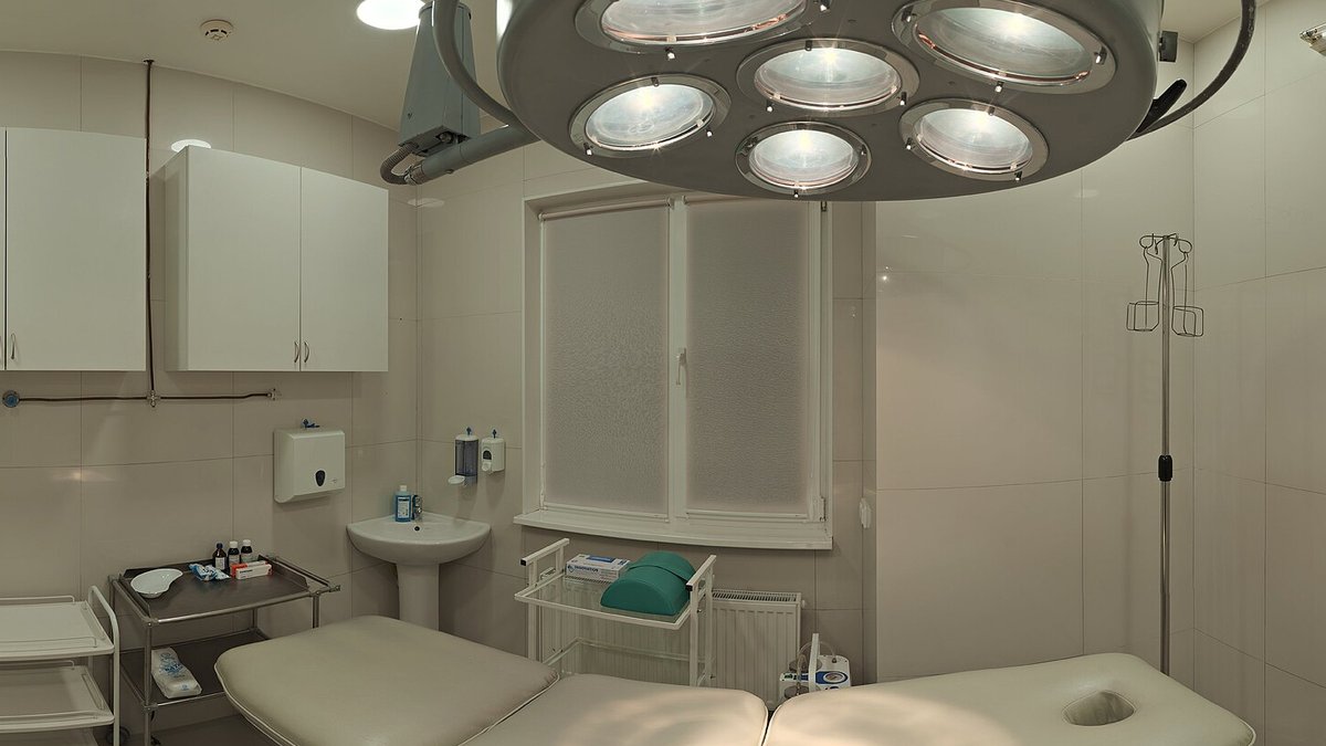 An empty treatment room with a padded table under a surgical light