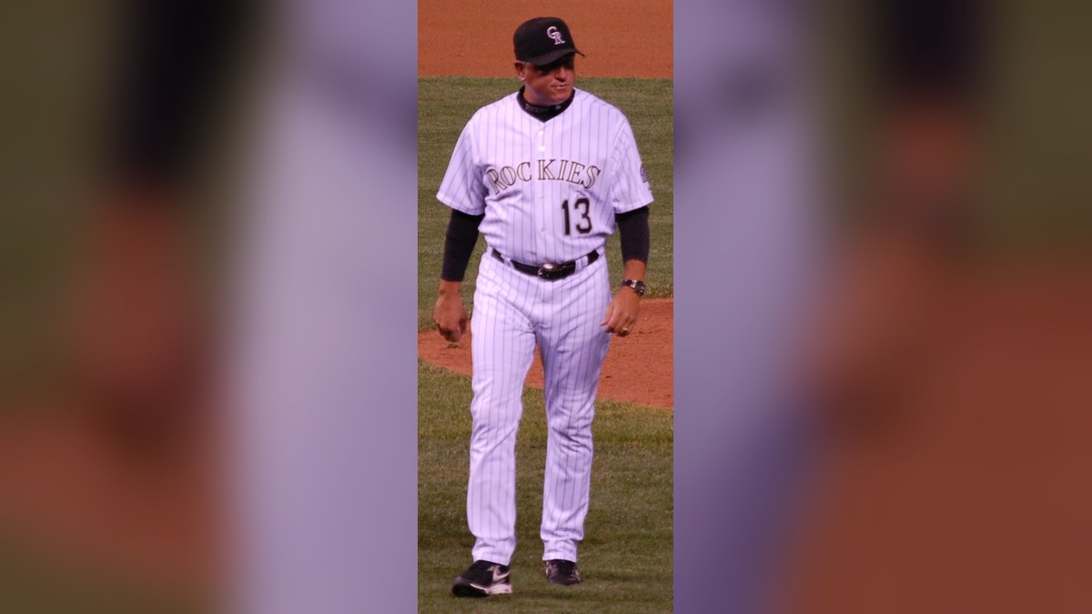 Clint Hurdle walking across the field in a white pinstriped Colorado Rockies No. 13 uniform and black cap