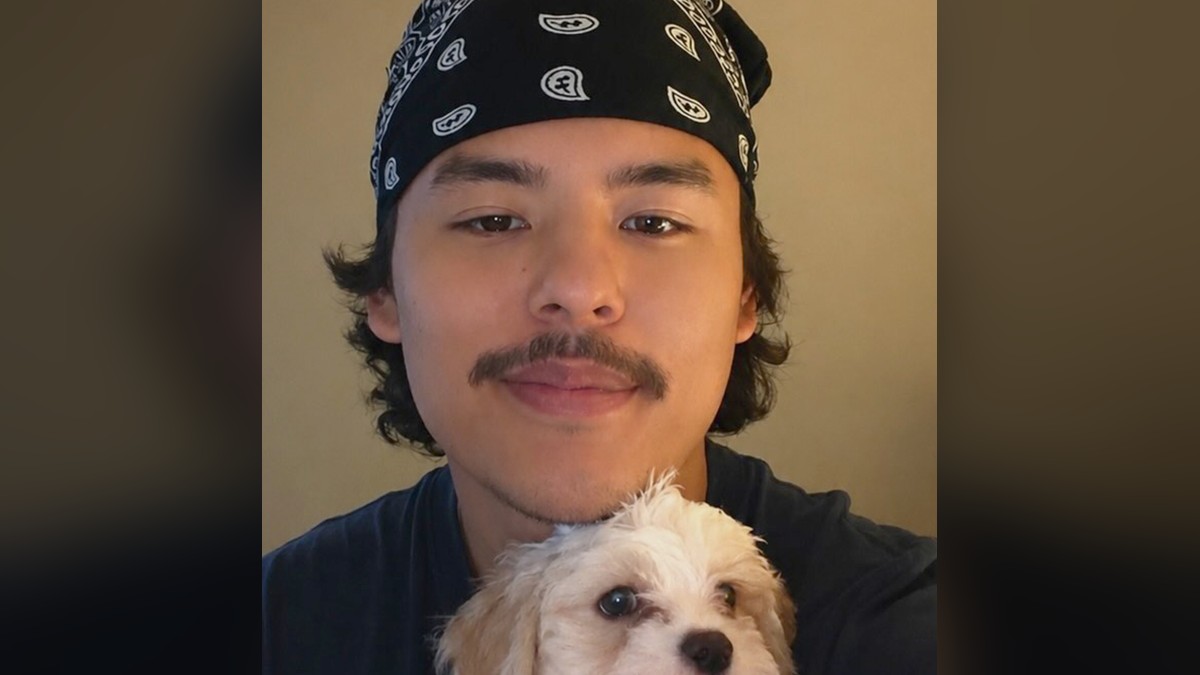 Collin Gosselin smiling in a black bandana while holding a small white dog