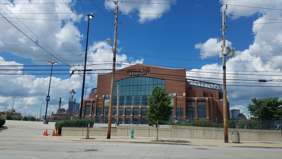 Lucas Oil Stadium in Indianapolis seen from a nearby parking lot under puffy clouds