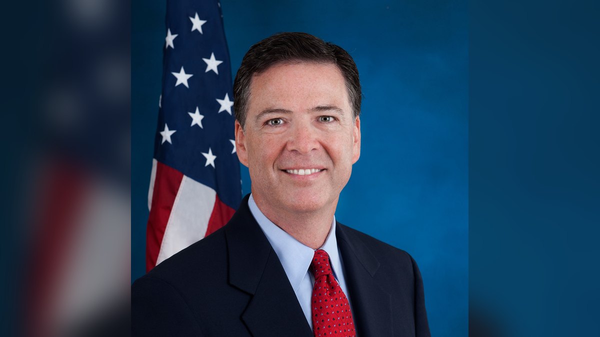James Comey smiling in his official FBI director portrait with an American flag behind him