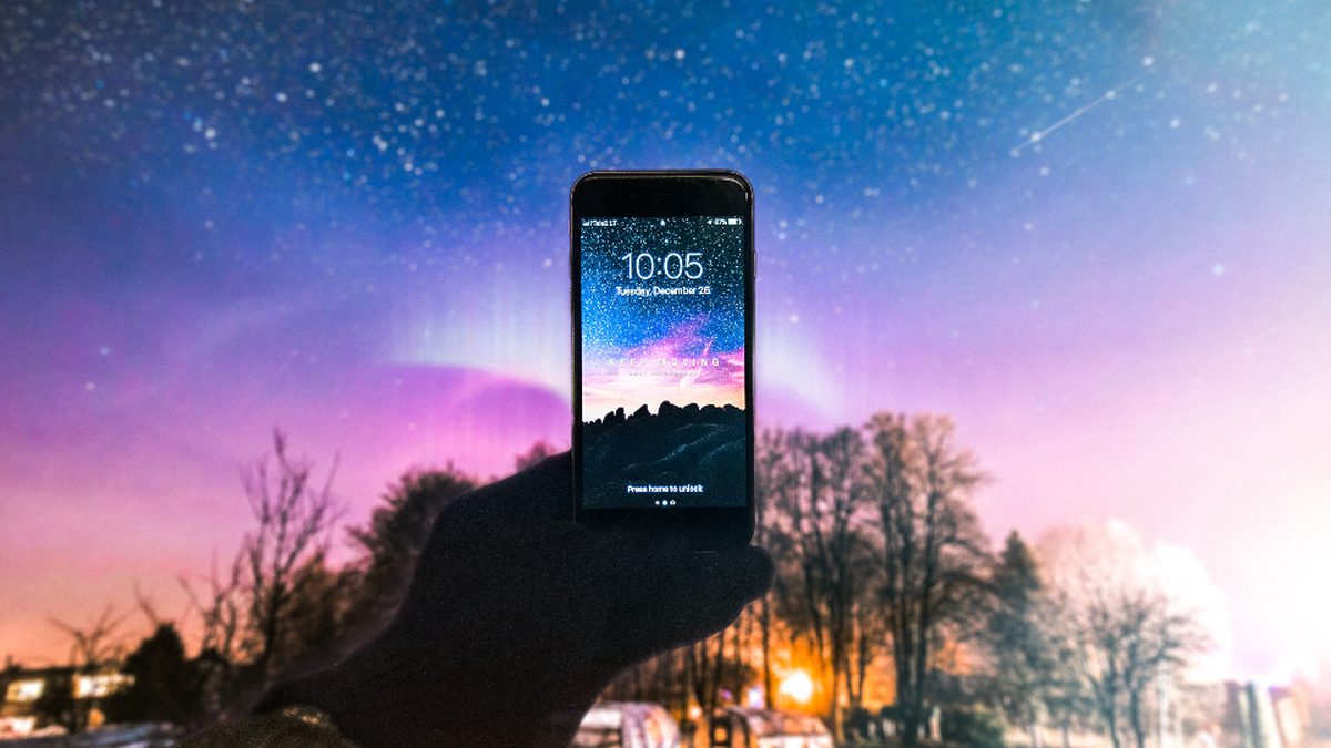 A hand holding up a lit smartphone against a starry night sky
