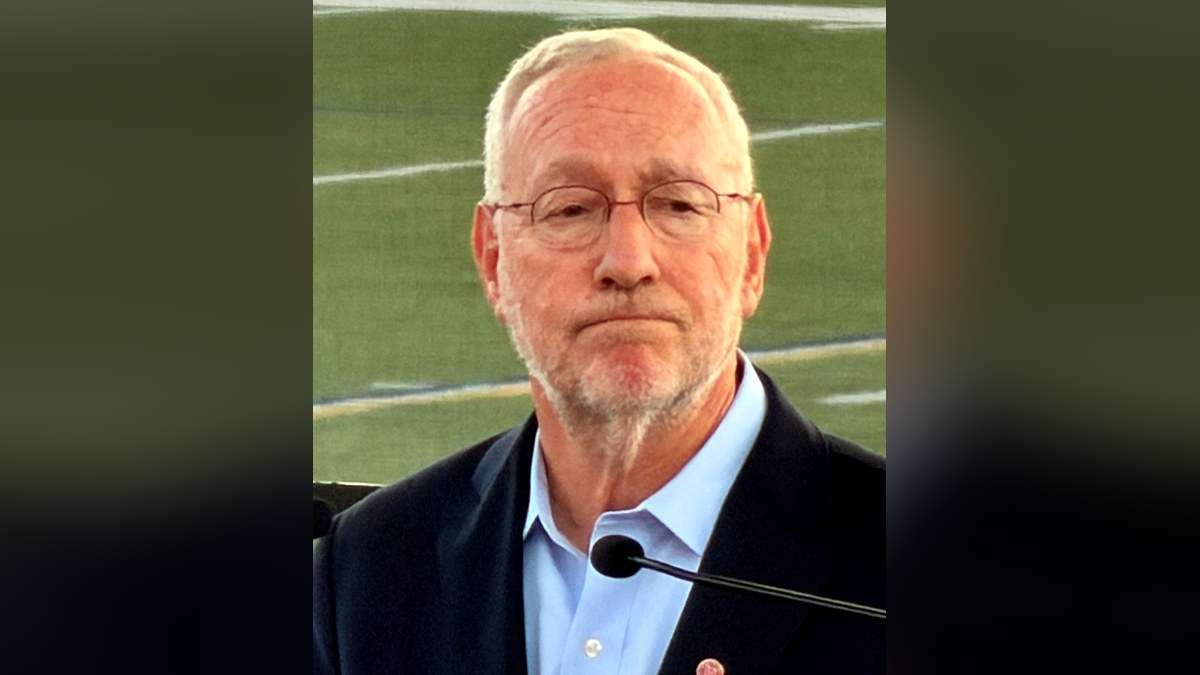 Cornell president Michael Kotlikoff in a navy blazer speaking at a microphone on a football field