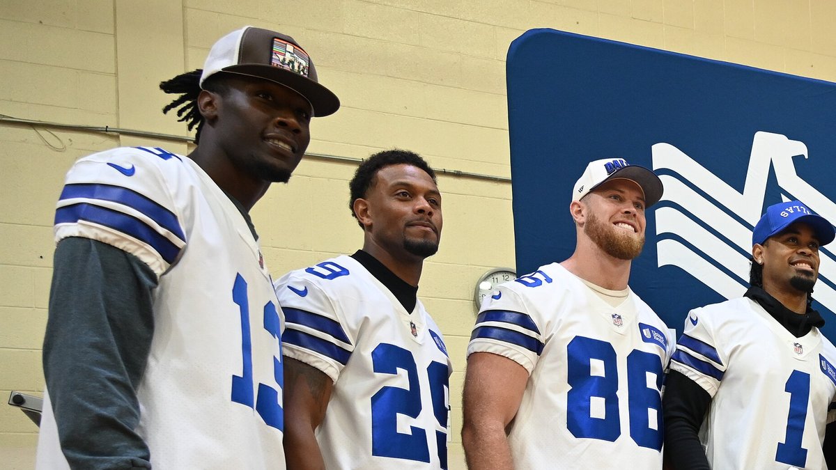 Dallas Cowboys players in white No. 13, 29, 86 and 1 jerseys standing together and smiling at a team visit